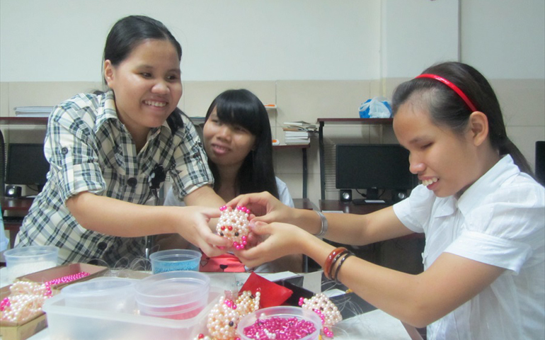 Maria Le Thi Anh Xuan, left, teaches visually impaired students how to make items by hand.
