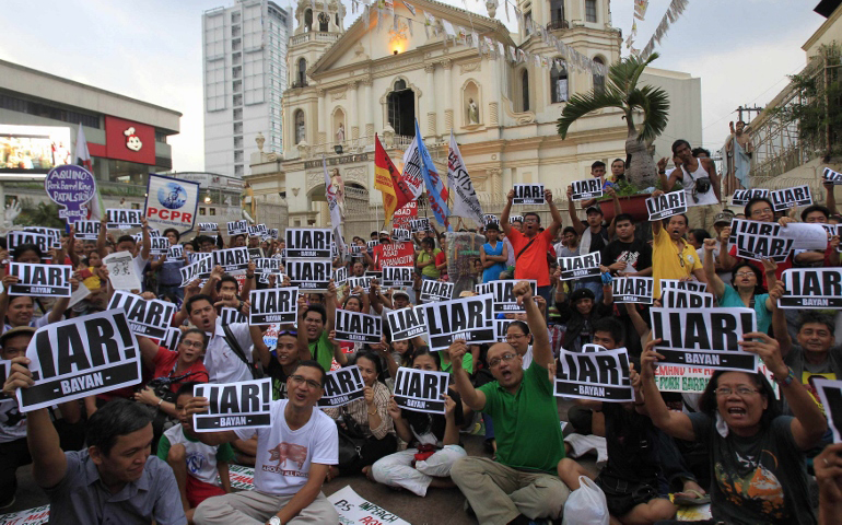 Protesters display placards in front of a Catholic church in Manila, the Philippines, as they watch President Benigno Aquino III address the nation in a live television broadcast July 14. (CNS/Reuters/Romeo Ranoco)