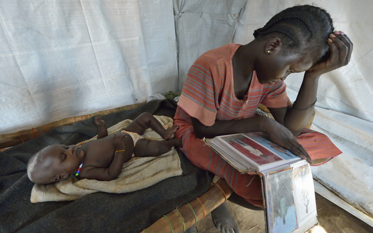 Nyanthem Mayol stares at photos of her relatives April 3 while her baby daughter, Sara, sleeps at her side in a temporary shelter near Ajuong Thok, South Sudan, to where they fled after fighting broke out in their home town of Bentieu in late 2013. (CNS/Paul Jeffrey)