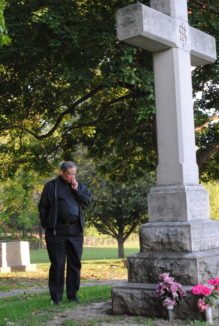 Chicago Auxiliary Bishop Joseph Perry takes a moment to reflect at the grave of Fr. Augustus Tolton at St. Peter's Cemetery, Quincy, Ill. Perry is the postulator for Tolton's sainthood cause. (NCR photo/Stephanie Yeagle)