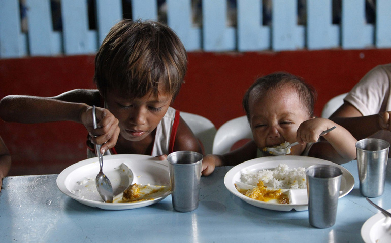A boy and his younger brother eat their free meals May 22 during a feeding program at a slum area in Manila, Philippines. (CNS/Reuters/Romeo Ranoco)