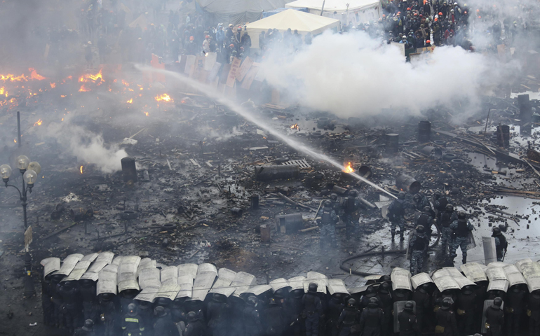 Riot police stand in formation as their colleagues attempt to extinguish a fire during clashes with anti-government protesters Wednesday in Independence Square in Kiev, Ukraine. (CNS/Reuters/Olga Yakimovich)