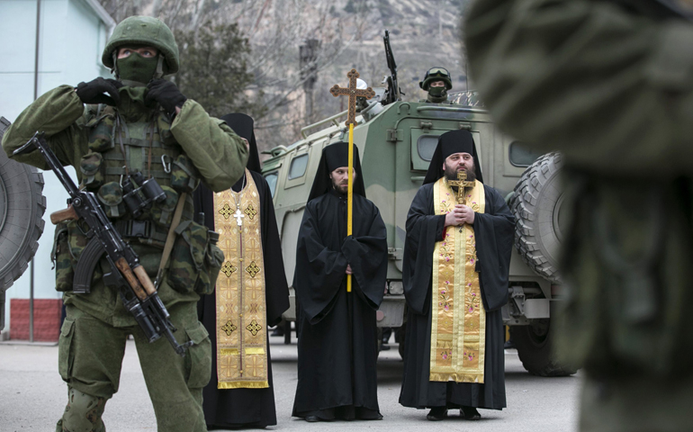 Orthodox clergymen pray next to armed servicemen near Russian army vehicles outside a Ukrainian border guard post in Ukraine's Crimean region March 1. (CNS/Reuters/Baz Ratner)