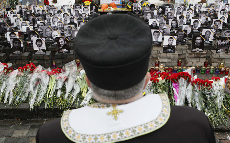 A clergyman stands near photos of people killed in Ukrainian protests in 2014 at a commemorating ceremony Friday in Kiev's Independence Square. (CNS/Reuters/Valentyn Ogirenko)