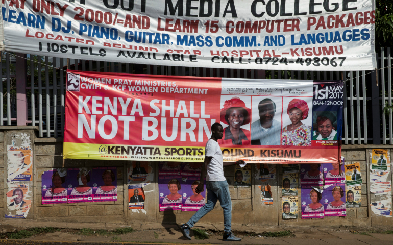 A man walks past a banner calling for prevention of violence during the primary elections April 20 in Kisumu, Kenya. (CNS photo/Baz Ratner, Reuters)