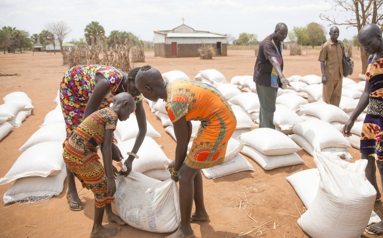 Young women help each other carry sacks of sorghum and beans March 17 after receiving them at a distribution center in Yirol, South Sudan. (CNS photo/courtesy David Mutua, CAFOD)