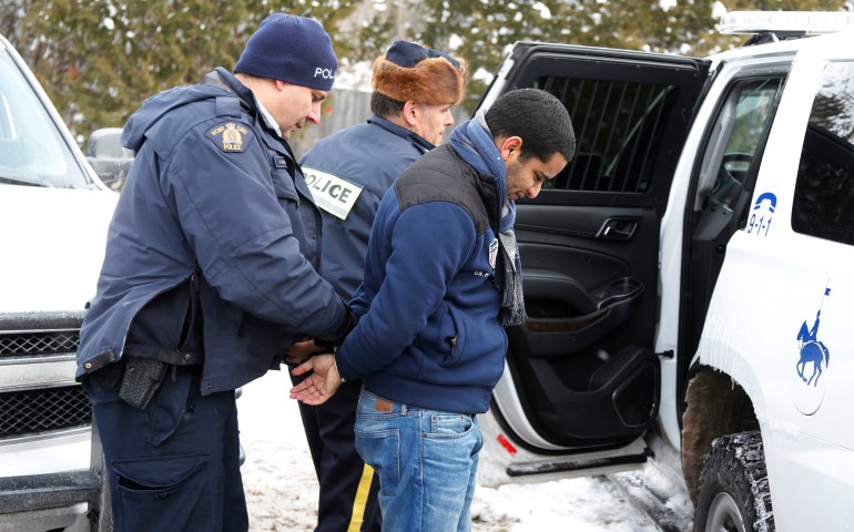 A man who told police he was from Mauritania is taken into custody Feb. 14 by Royal Canadian Mounted Police officers after walking across the U.S.-Canada border into Quebec. (CNS photo/Christinne Muschi, Reuters)