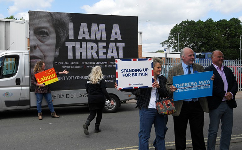 Labour Party supporters, rear, stand next to an electronic billboard behind Conservative Party supporters, front, outside a campaign event attended by Britain's Prime Minister Theresa May in Norwich, Britain, on June 7, 2017. (Reuters/Toby Melville)