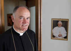 Bishop Bernard Fellay, superior of the Society of St. Pius X, is pictured near a photo of Pope Benedict XVI at the society's headquarters in Menzingen, Switzerland, May 11. (CNS/Paul Haring)