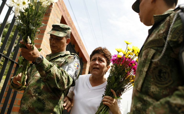 A woman and soldier place flowers in front of an army headquarter in early April in Cali, Colombia. in honor of the 11 members of Colombian army who died after an attack by Revolutionary Armed Forces of Colombia, FARC, rebel group. (CNS photo/Christian Escobar Mora, EPA)