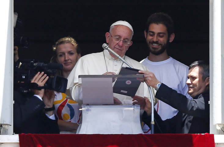 Pope Francis is flanked by two Polish youths as he uses an iPad to make the first online registration for the next 2016 World Youth Day in Poland, as he leads the Angelus prayer from the window of the Apostolic Palace in St. Peter’s Square at the Vatican on July 26, 2015. Photo courtesy of Reuters/Max Rossi