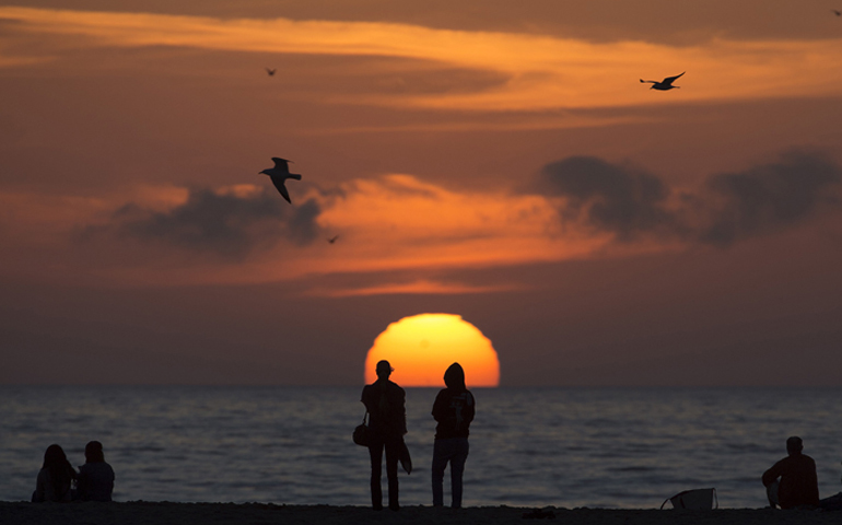 People sit on the beach and watch the sun set as seagulls fly overhead in Santa Monica, Calif. (REUTERS/Carlo Allegri)