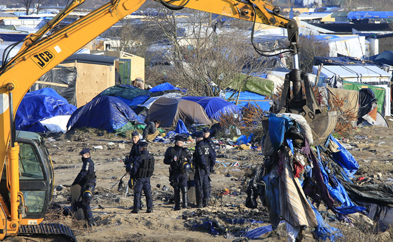 French police officers secure the area as a crane is used to clear dismantled shelters of the camp known as the “Jungle”, a squalid sprawling camp in Calais, northern France, on January 20, 2016. (Reuters/Pascal Rossignol)