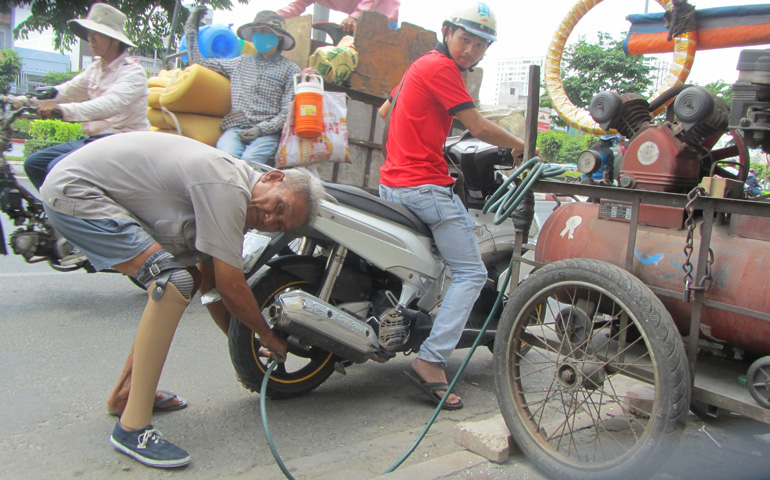 South Vietnamese veteran Dinh Van Hoang lives on the sidewalk and has made a living filling motorbike tires for years. (Photos by Mary Nguyen)