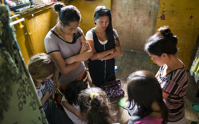 Three sister missionaries kneel in prayer with a family in the Philippines. (Courtesy of Intellectual Reserve, Inc.