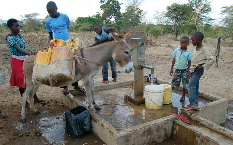 Eunice Wambua, left, and Joel Kimeu wait for cans to fill at a well near Mango, Kenya, on March 17, 2017. Wambua says life is much easier for her since the drilling of the well. (RNS photo Fredrick Nzwili)