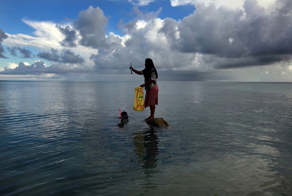 In this May 25, 2013, file photo, a woman holds a fish caught by her husband off South Tarawa in the central Pacific island nation of Kiribati. (CNS/David Gray, Reuters)
