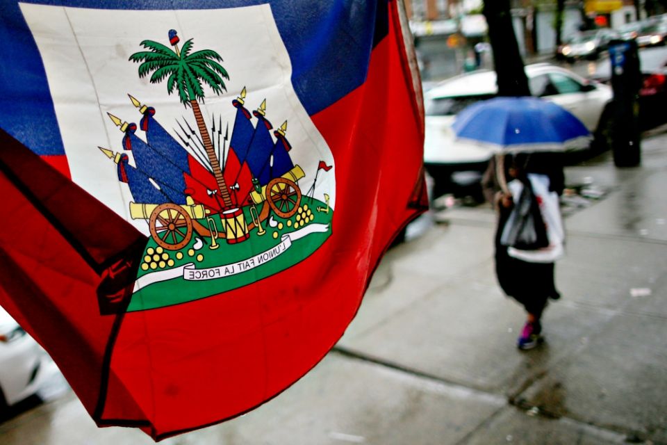 A flag from Haiti hangs outside a store as a woman walks with an umbrella May 13 in Brooklyn, New York. (CNS/Reuters/Eduardo Munoz)