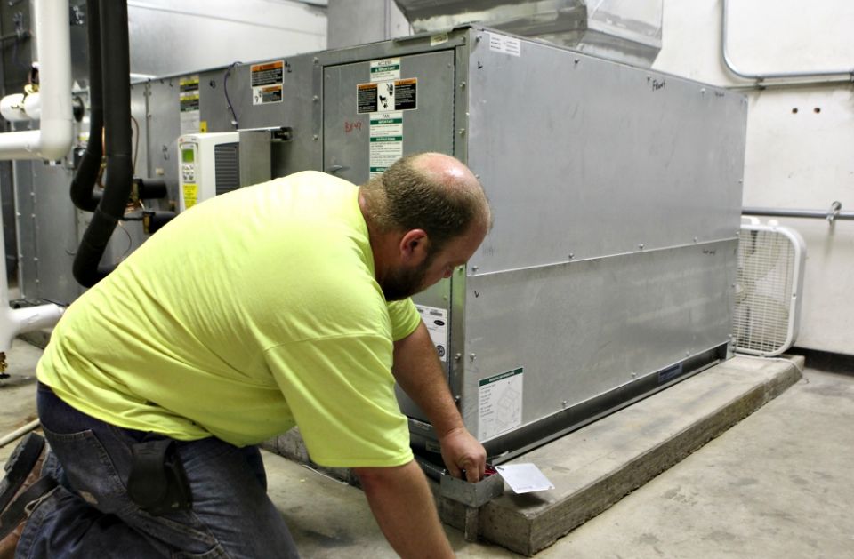 Technician Brian Wayson of AirStream Mechanical in Cincinnati checks wiring on a high-efficiency air conditioning unit at St. John Fisher Church in Newtown, Ohio, Aug. 17, retrofitting the unit under the Catholic Energies program. (CNS/Dennis Sadowski)