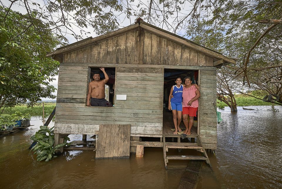 Juscelina Silva Batista (right), 54, her daughter Geovana Batista de Sousa, 11, and her partner Cantidio Rego, 69, stand in their home in a seasonally flooded area of the Amazon River near Santarem, Brazil, in 2019. (CNS/Paul Jeffrey)