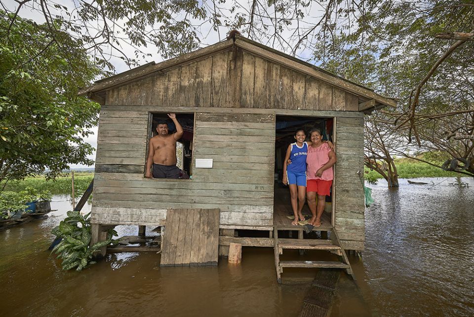 A family stands in their home in a seasonally flooded area of the Amazon River near Santarem, Brazil. Juscelina Silva Batista (right), 54, her daughter Geovana Batista de Sousa, 11, and her partner Cantidio Rego, 69, stand in their home in a seasonally flooded area of the Amazon River near Santarem, Brazil, in 2019. (CNS/Paul Jeffrey)