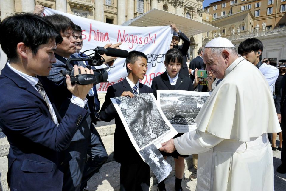 Pope Francis examines photos of the aftermath of the 1945 atomic bombing of Japan as he greets members of the Hiroshima and Nagasaki Youth Peace Messengers at his weekly general audience June 19. (CNS/Vatican Media)