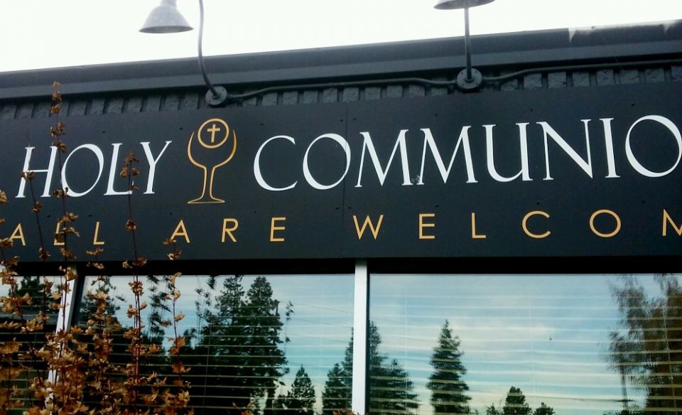 Attached to a strip mall storefront, a sign proclaims "All Are Welcome" at Holy Communion Church in Bend, Oregon. (NCR photo/Peter Feuerherd)