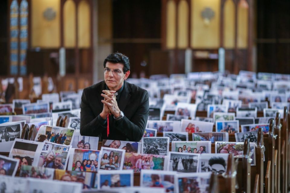 Fr. Reginaldo Manzotti prays during Mass with photos of his parishioners taped to the pews in the Shrine of Our Lady of Guadalupe in Curitiba, Brazil, March 21. (CNS/Reuters/Rodolfo Buhrer)