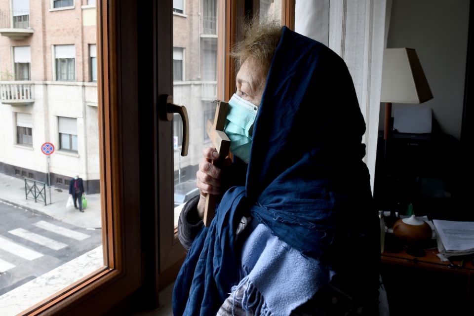 A woman wearing a protective face mask kisses a cross as she prays from the window of her home in Turin, Italy, March 25. (CNS/Reuters/Massimo Pinca)