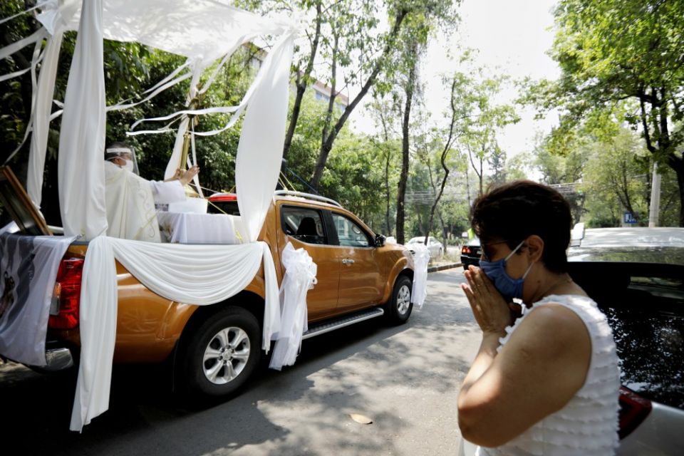 A woman prays as Fr. Angel Lauro Sánchez, pastor of the Lady of the Rosary Church in Mexico City, blesses people while riding in a pickup truck with a monstrance April 19 during the COVID-19 pandemic. (CNS/Reuters/Luis Cortes)