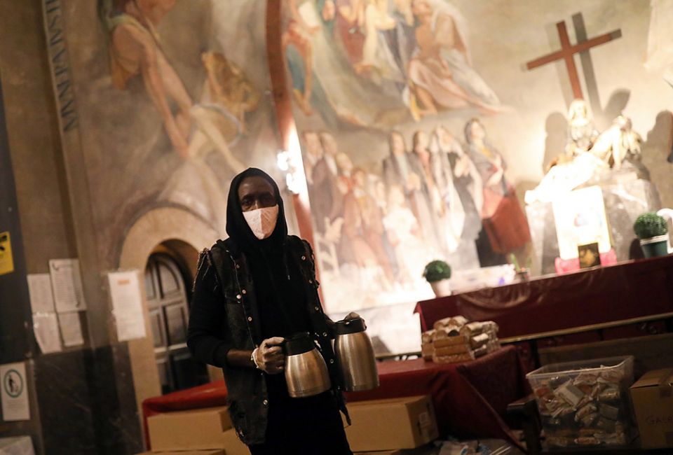 A volunteer carries coffee for people waiting for a free meal at the Church of Santa Anna in Barcelona, Spain, April 21, 2020, during the COVID-19 pandemic. (CNS/Reuters/Nacho Doce)