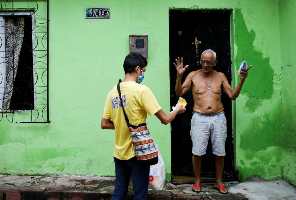 Seminarian Renan Alberto Lima de Oliveira, 21, assigned to Our Lady of Perpetual Help Catholic Church in Manaus, Brazil, delivers a protective mask to a resident in one of the city's slums May 21 to minimize the spread of COVID-19. (CNS/Reuters)