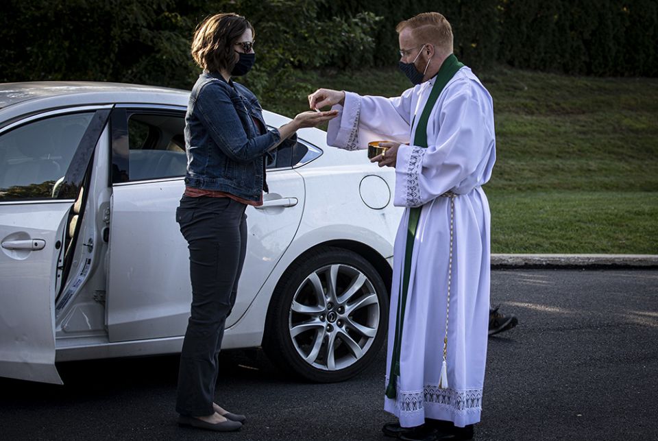 Fr. Mark Searles, a resident priest at St. Thomas More Catholic Church in Allentown, Pennsylvania, wears a mask while giving Communion to a parishioner following an Oct. 2, 2020, Mass celebrated in the parish parking lot. (CNS/Chaz Muth)