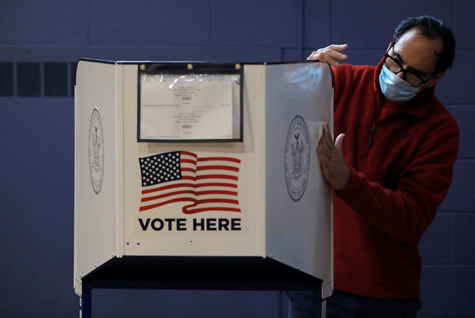 A man sanitizes a voting booth to fight the spread of the coronavirus disease at a polling station Oct. 25 on Staten Island, New York. (CNS/Reuters/Andrew Kelly)