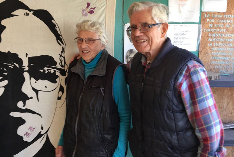 Mercy Sister Betty Campbell and Carmelite Fr. Peter Hinde pose next to an illustration of St. Oscar Romero in a 2019 photo in Ciudad Juarez, Mexico. Hinde died from complications due to COVID-19 Nov. 19, at the age of 97. (CNS/Julie Bourbon, courtesy of t
