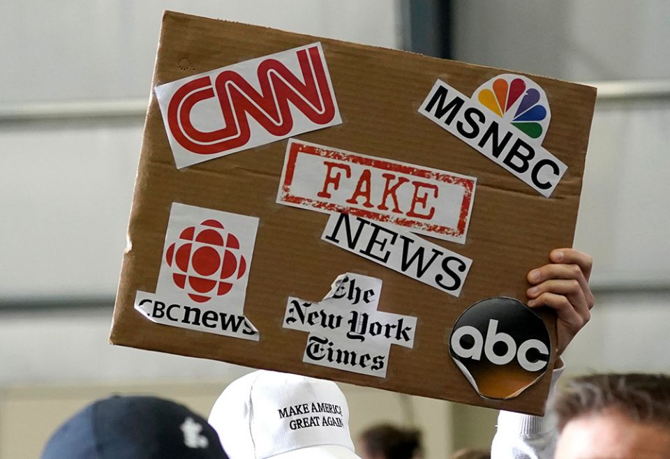 A sign showing major news organizations along with the words "fake news" is held up as then-U.S. President Donald Trump speaks at a rally in Washington, Michigan April 28, 2018. (CNS/Reuters/Joshua Roberts)