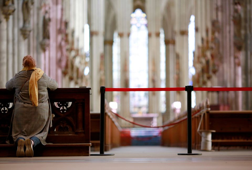 A woman prays alongside a barrier inside the Cologne Cathedral in Germany March 15, 2020, during the COVID-19 pandemic. (CNS/Reuters/Thilo Schmuelgen)
