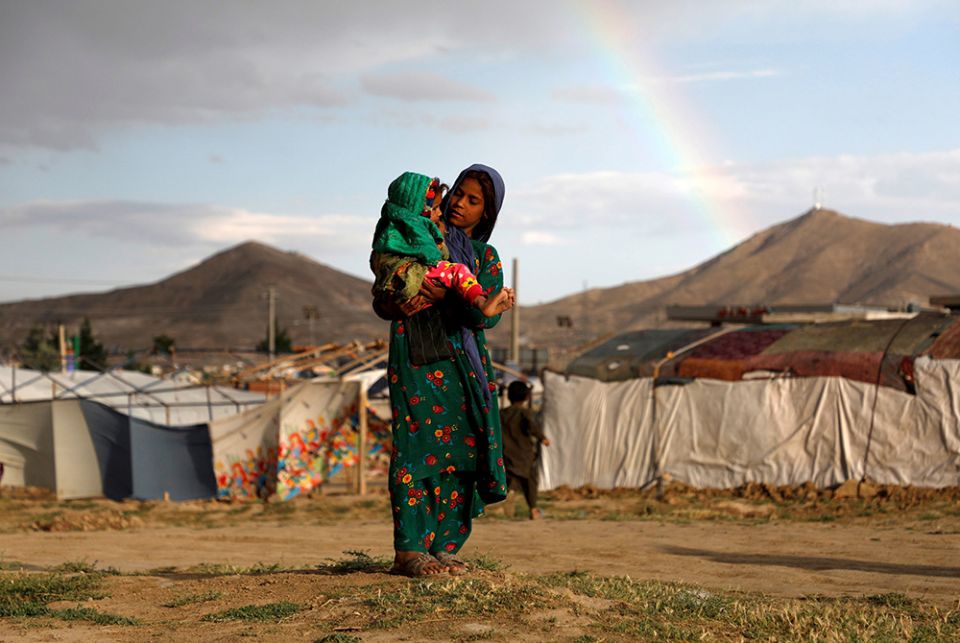 A young internally displaced Afghan woman carries a child as a rainbow forms near their shelter at a camp on the outskirts of Kabul June 20, 2019. (CNS/Reuters/Omar Sobhani)