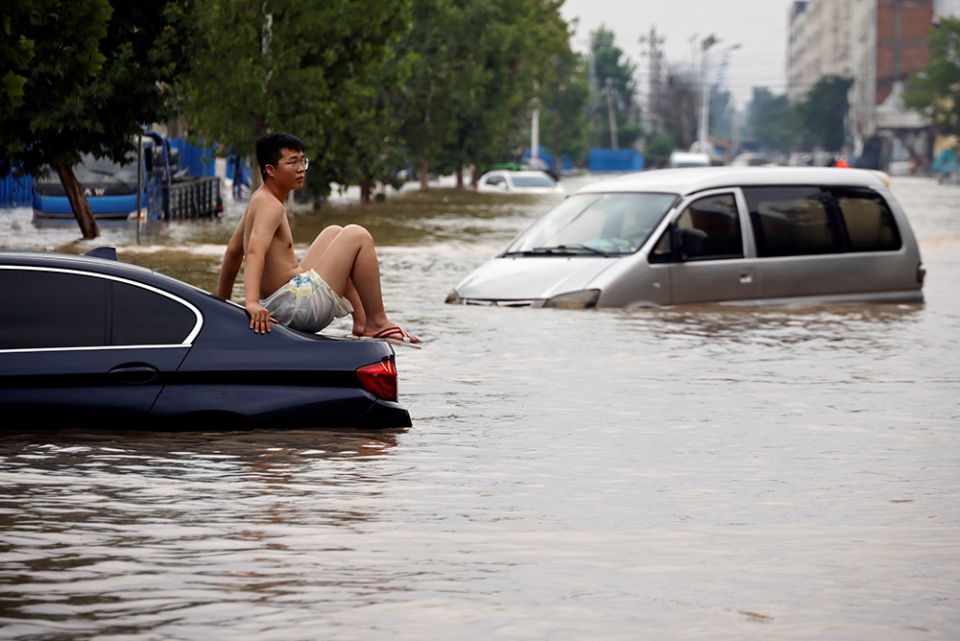 A man sits on a stranded vehicle on a flooded road following heavy rainfall in Zhengzhou, China, July 22. (CNS/Reuters/Aly Song)