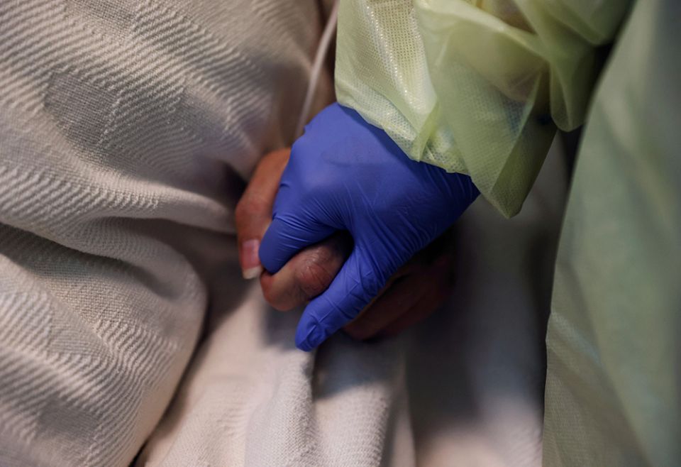 A woman at Madison Memorial Hospital in Rexburg, Idaho, holds the hand of a COVID-19 patient in her isolation room Oct. 28, 2021. (CNS/Reuters/Shannon Stapleton)