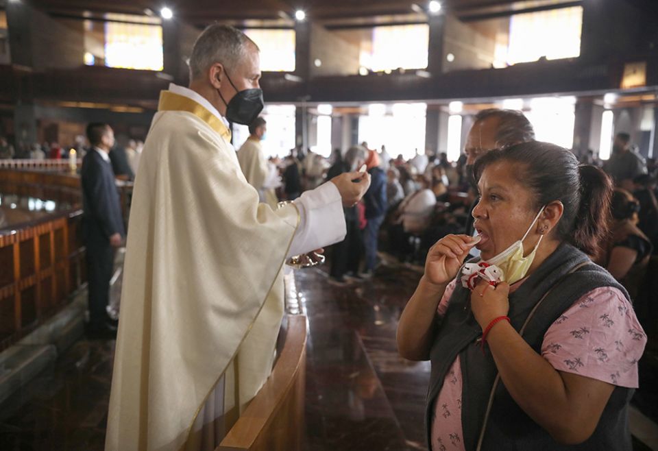 A woman lowers her protective mask after receiving Communion during the opening Mass of the Ecclesial Assembly of Latin America and the Caribbean at the Basilica of Our Lady of Guadalupe Nov. 21, 2021, in Mexico City. (CNS/Emilio Espejel)