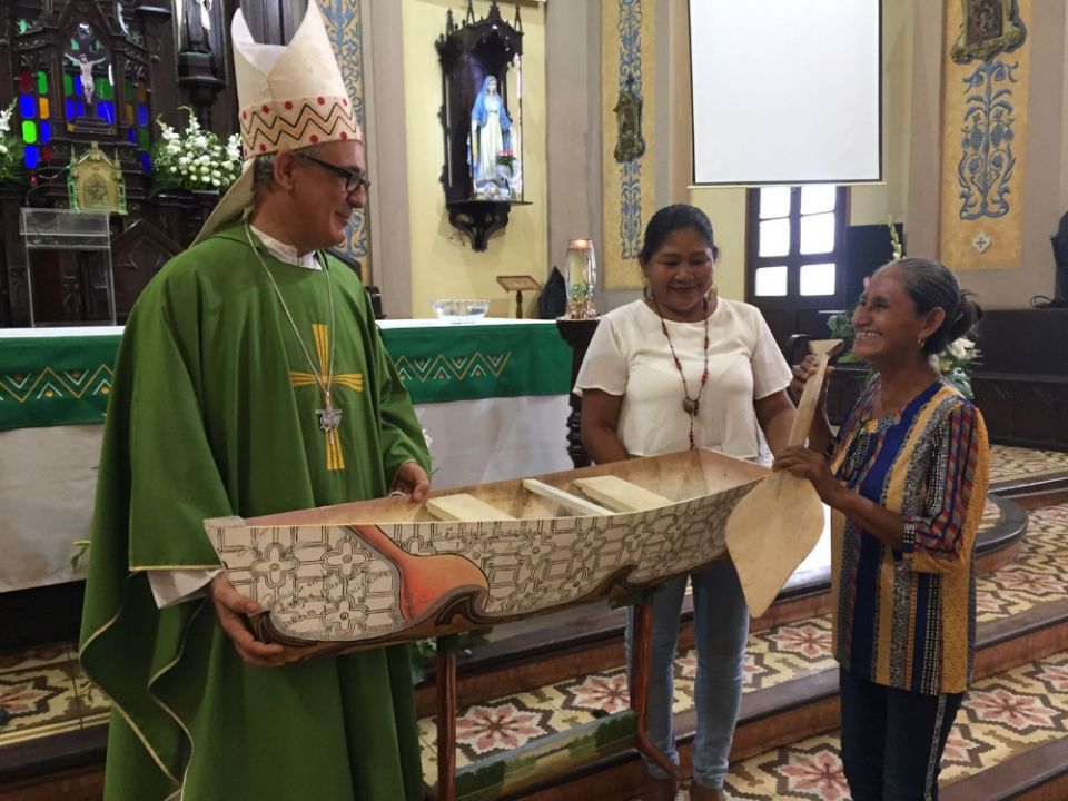 Bishop Miguel Angel Cadenas of Iquitos, Peru, talks with Emilsen Flores (right) and Mari Luz Cañaquiri, leaders of a Kukama women's organization, after a Feb. 13, 2022, Mass in Iquitos. The canoe model was presented during the offertory. (CNS/Barbara Fras
