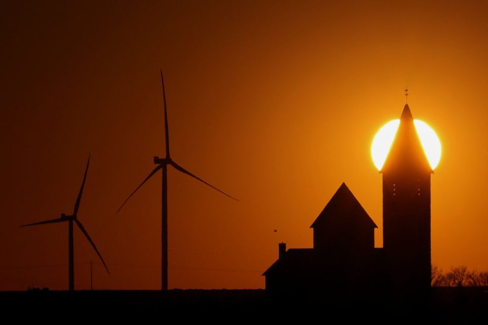 Power-generating windmill turbines and a church are pictured during sunset at a wind park near Cambrai, France, March 18, 2022. (CNS/Reuters/Pascal Rossignol)