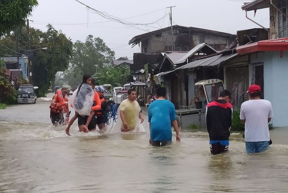A member of the Philippine Coast Guard carries a young girl April 10, 2022, as they walk on a flooded road after Tropical Storm Megi hit Leyte Island. (CNS/Reuters/Philippine Coast Guard Handout)