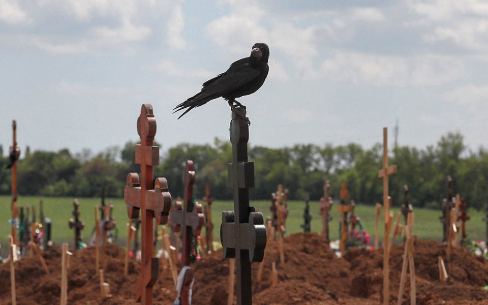 A bird sits on a cross amid newly made graves at a cemetery near Mariupol, Ukraine, May 15, during the Ukraine-Russia conflict. (CNS/Reuters/Alexander Ermochenko)