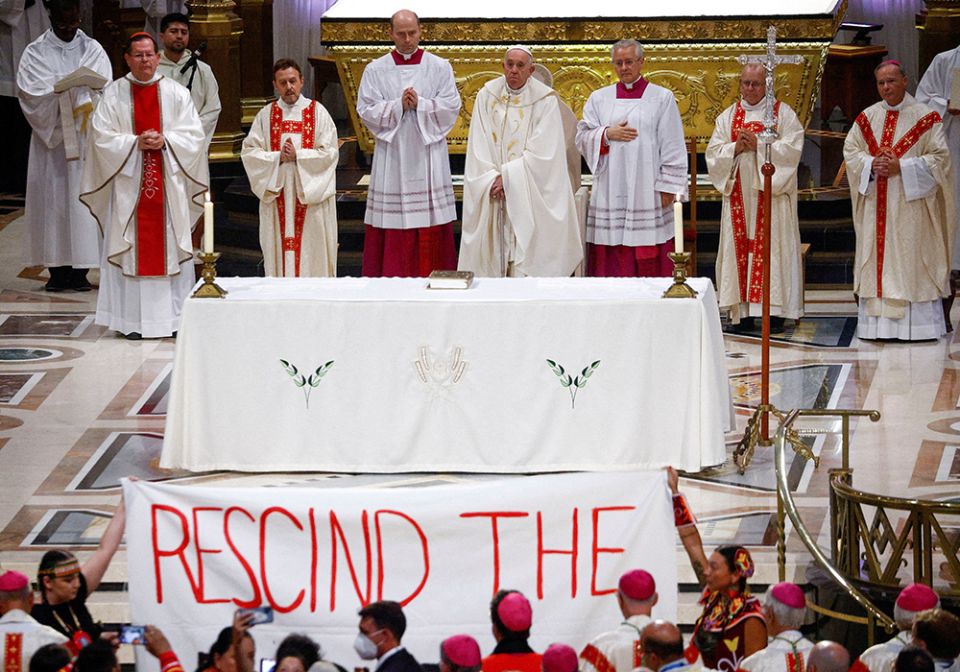 Indigenous people hold a banner calling on Pope Francis to "rescind the doctrine" during a papal Mass at the Basilica of Ste. Anne de Beaupré July 28 in Quebec. (CNS/Reuters/Guglielmo Mangiapane)
