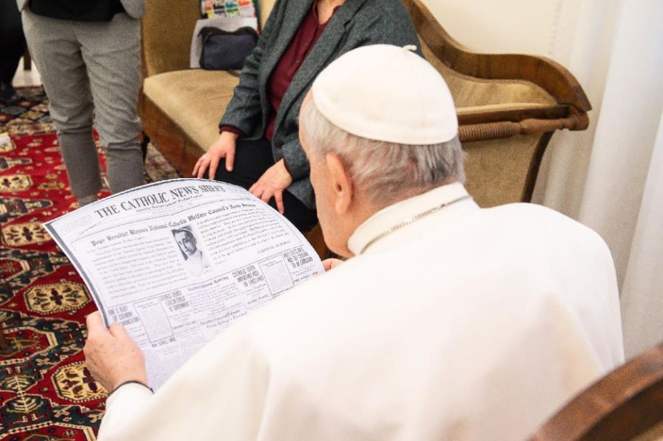 Pope Francis looks at a copy of the April 11, 1920, edition of the Catholic News Sheet during a meeting with members of the Catholic News Service Rome bureau at the Vatican Feb. 1, 2021.