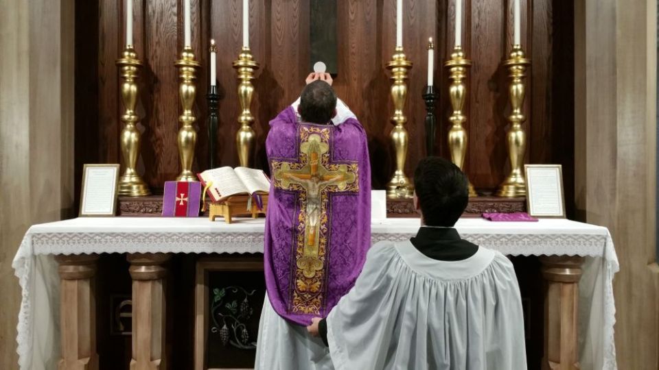 A priest elevates the Eucharist after consecrating it during a Latin Mass. (Creative Commons/ Andrew Gardner)