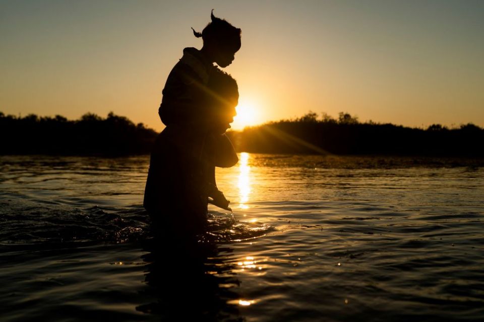 A migrant seeking asylum in the U.S. carries a child on his shoulder Sept. 20 as they cross the Rio Grande back into Mexico near the International Bridge between Mexico and the U.S. (CNS/Reuters/Go Nakamura)