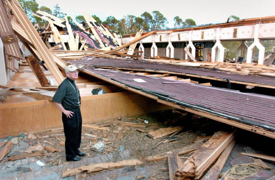 Archbishop Alfred C. Hughes, who was head of the New Orleans Archdiocese at the time, stands amid the rubble of the collapsed roof of Our Lady of Lourdes Church in Slidell, La., after Hurricane Katrina in 2005.(CNS/Clarion Herald/Frank J. Methe)